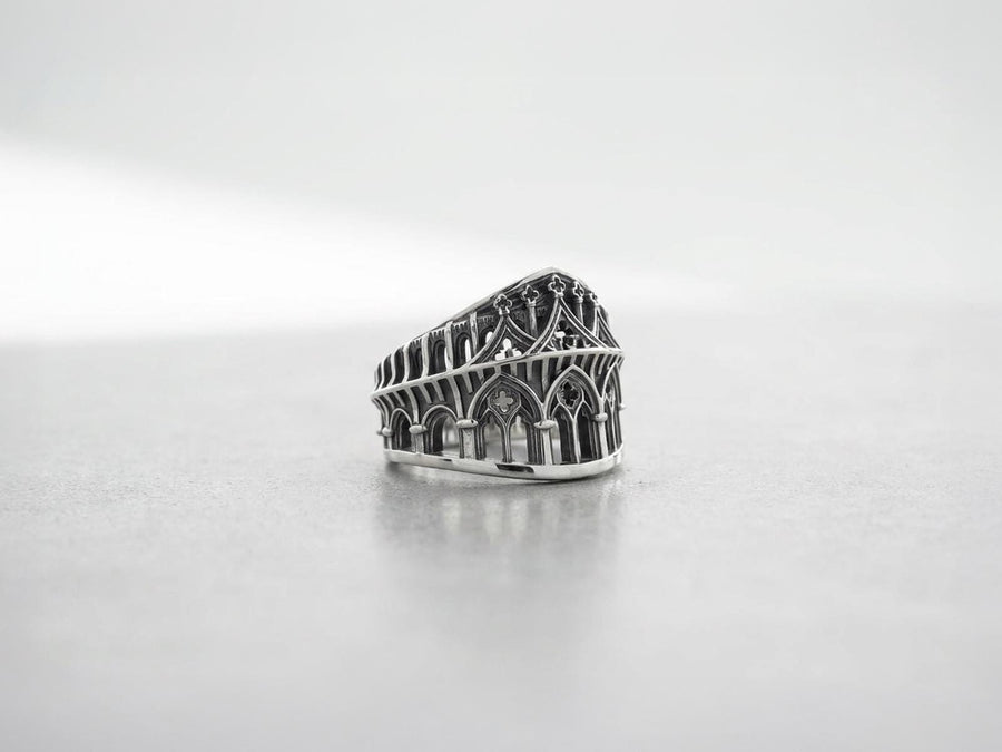 This striking artisan ring perfectly captures the monumental scale of medieval architecture. Bright studio lighting illuminates the polished silver arches and columns, contrasting beautifully with the deep, dark oxidation inside the hollow windows and recesses. Crafted from premium solid 925 sterling silver, this wide architectural band demonstrates the visual impact of an antiqued patina. Heavy sulfur oxidation settles into the intricate crevice