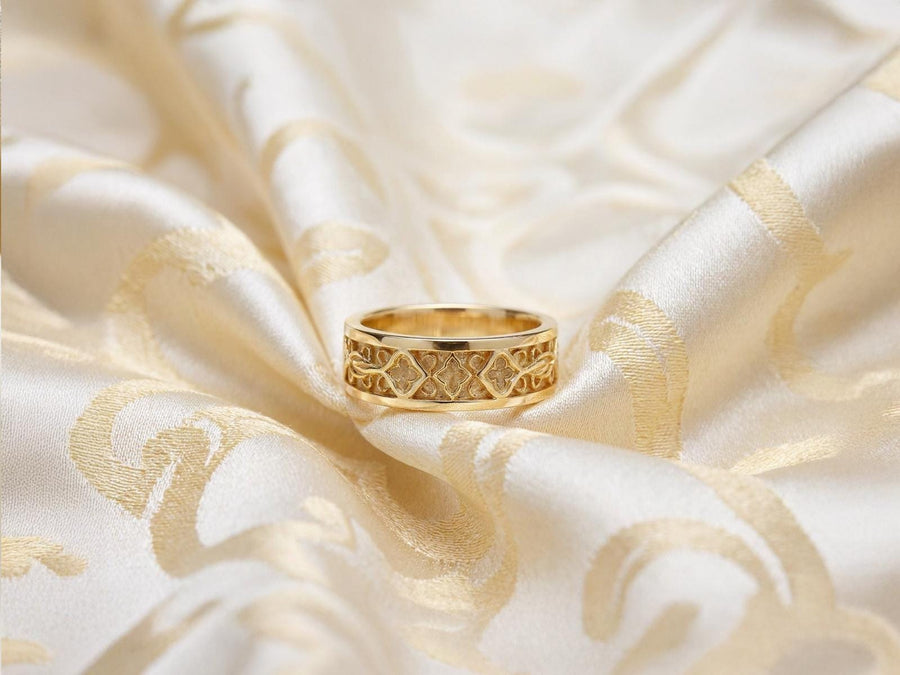 A close-up studio photograph of a matching 925 sterling silver gothic wedding ring set on a grey surface. The wide mens band and the delicate womens engagement ring both feature intricate medieval tracery and carved quatrefoils - highlighted by a dark oxidized background. This striking artisan bridal set perfectly captures the monumental scale of medieval architecture. Bright lighting illuminates the polished silver edges and the sparkling oval g