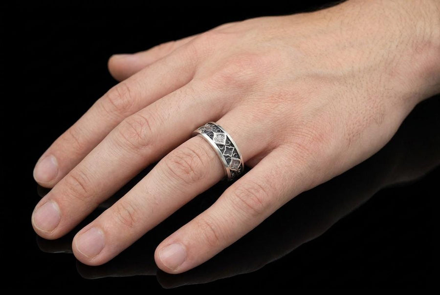 A close-up studio photograph of a matching 925 sterling silver gothic wedding ring set on a grey surface. The wide mens band and the delicate womens engagement ring both feature intricate medieval tracery and carved quatrefoils - highlighted by a dark oxidized background. This striking artisan bridal set perfectly captures the monumental scale of medieval architecture. Bright lighting illuminates the polished silver edges and the sparkling oval g