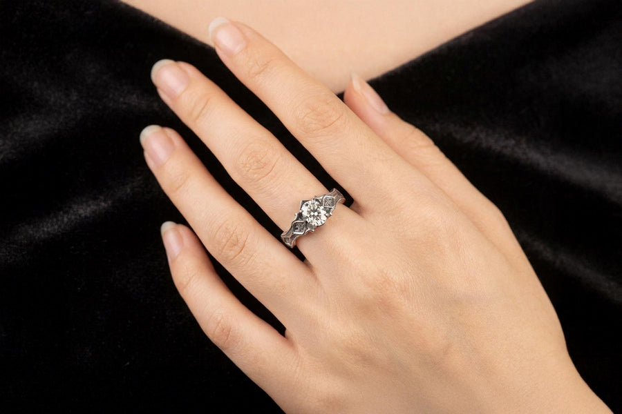 A close-up studio photograph of a matching 925 sterling silver gothic wedding ring set on a grey surface. The wide mens band and the delicate womens engagement ring both feature intricate medieval tracery and carved quatrefoils - highlighted by a dark oxidized background. This striking artisan bridal set perfectly captures the monumental scale of medieval architecture. Bright lighting illuminates the polished silver edges and the sparkling oval g