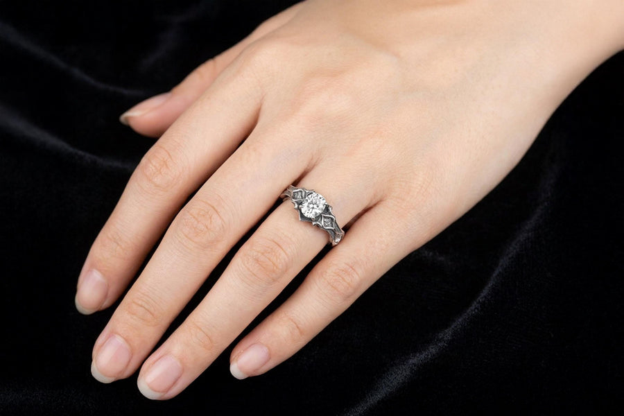 A close-up studio photograph of a matching 925 sterling silver gothic wedding ring set on a grey surface. The wide mens band and the delicate womens engagement ring both feature intricate medieval tracery and carved quatrefoils - highlighted by a dark oxidized background. This striking artisan bridal set perfectly captures the monumental scale of medieval architecture. Bright lighting illuminates the polished silver edges and the sparkling oval g