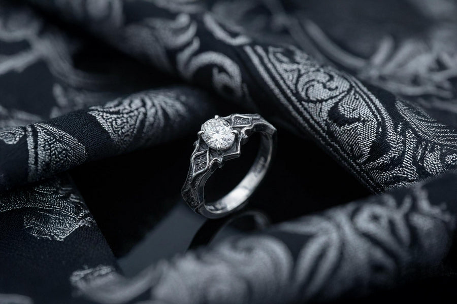 A close-up studio photograph of a matching 925 sterling silver gothic wedding ring set on a grey surface. The wide mens band and the delicate womens engagement ring both feature intricate medieval tracery and carved quatrefoils - highlighted by a dark oxidized background. This striking artisan bridal set perfectly captures the monumental scale of medieval architecture. Bright lighting illuminates the polished silver edges and the sparkling oval g