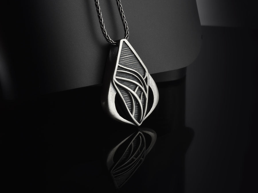 Embrace the fluid elegance of dark fantasy and organic architecture. This sweeping silver teardrop pendant is a striking statement piece, designed for those who are captivated by the seamless blend of natural forms and futuristic biomechanics. Crafted from solid 925 sterling silver, this amulet offers a sophisticated touch of avant-garde mystique to any alternative look. A close-up studio photograph of a 925 sterling silver sci-fi pendant resting