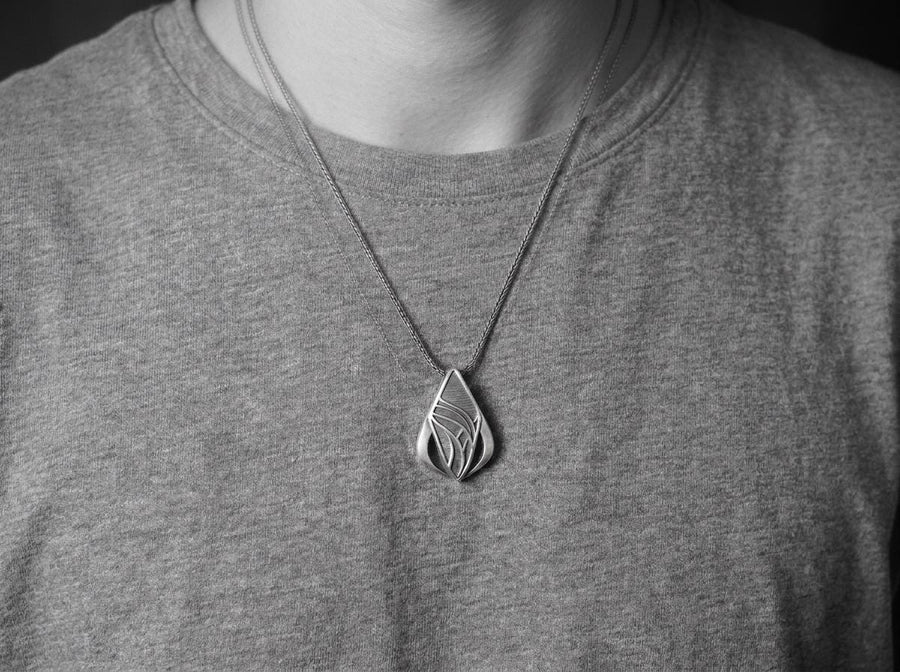 Embrace the fluid elegance of dark fantasy and organic architecture. This sweeping silver teardrop pendant is a striking statement piece, designed for those who are captivated by the seamless blend of natural forms and futuristic biomechanics. Crafted from solid 925 sterling silver, this amulet offers a sophisticated touch of avant-garde mystique to any alternative look. A close-up studio photograph of a 925 sterling silver sci-fi pendant resting