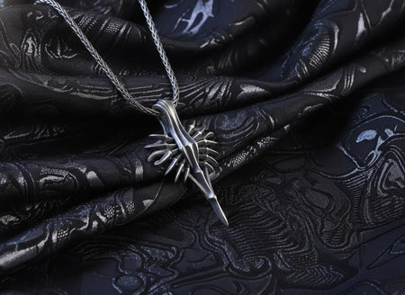 Dark sci-fi silver spear pendant resting on dark patterned fabric, highlighting its biomechanical spikes and oxidized finish.