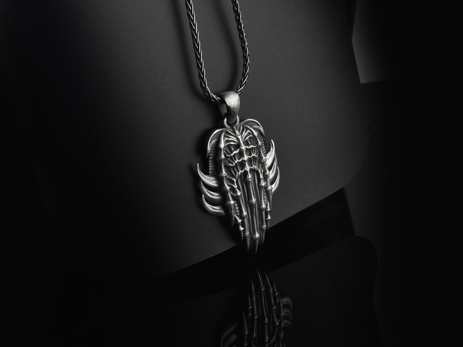Close up of a man's hand holding a highly detailed gothic spine amulet, showing sharp silver claws and bone textures.