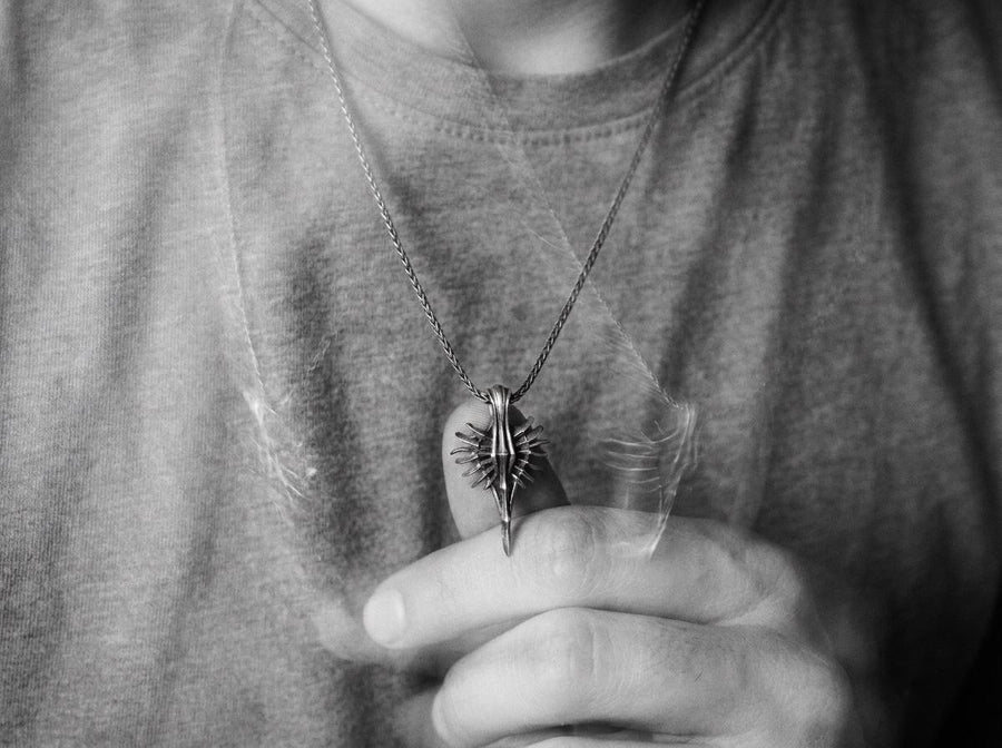 Close-up of a man's hand holding a solid sterling silver alien weapon necklace, showing the sharp elongated drop.