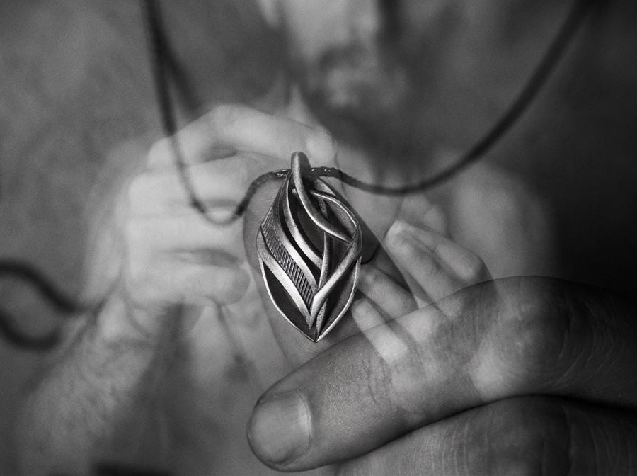 Dark fantasy silver teardrop pendant resting on black fabric, showing sweeping organic lines and an oxidized micro-ribbed background.