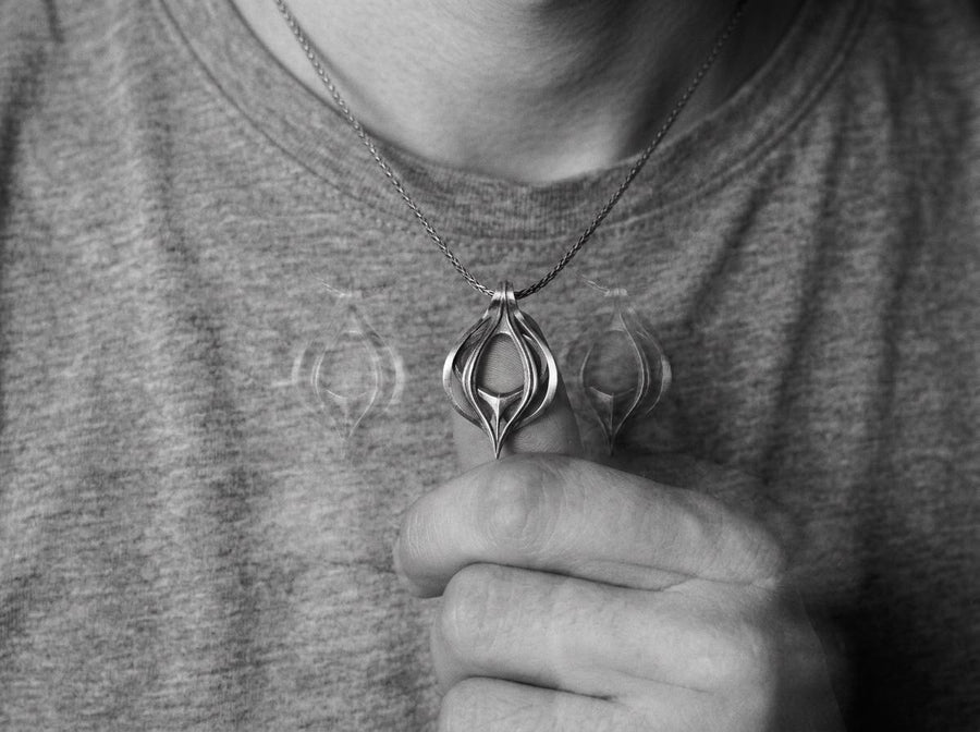 Oxidized biomechanical teardrop pendant suspended on an anchor chain, emphasizing its airy cut-out structure.
