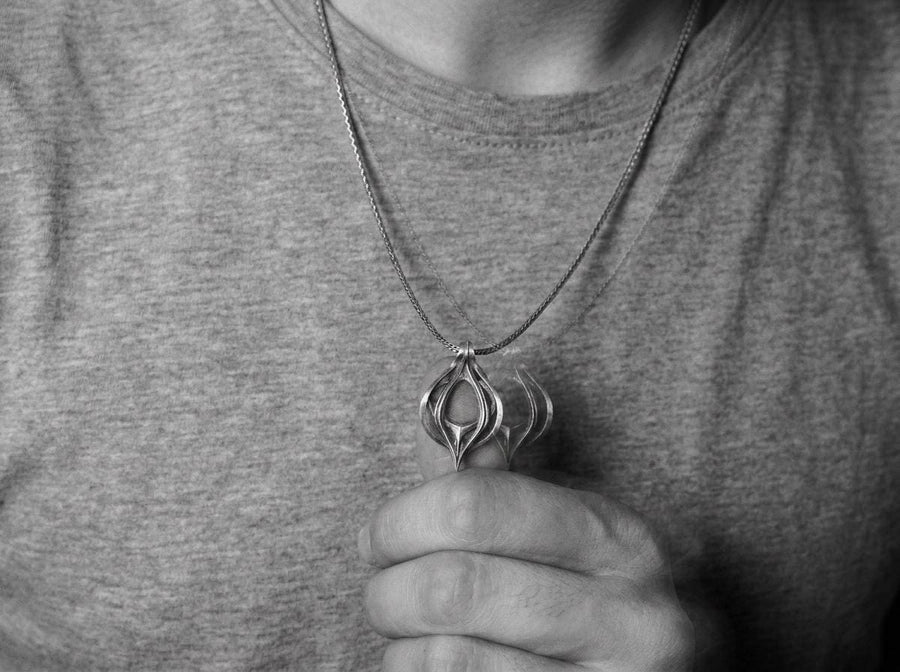 Oxidized biomechanical teardrop pendant suspended on an anchor chain, emphasizing its airy cut-out structure.