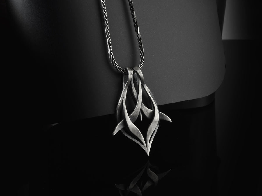 Solid sterling silver esoteric dagger drop charm held in hand, emphasizing the aggressive yet elegant lines. Close up of a man's fingers holding an abstract gothic spike amulet, highlighting the openwork silver design. Exceptional silversmithing is evident in this oxidized silver avant-garde necklace. The relief work perfectly balances the sharp lower points with smooth, sweeping interlaced upper curves. A bold modern statement piece for alte