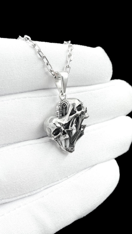 A side-profile view of the silver skull pendant showcases the breathtaking depth of the sculpted elements. The skulls appear stretched and elongated, morphing into each other. Dark oxidation heavily shadows the deeply recessed areas of the bone.