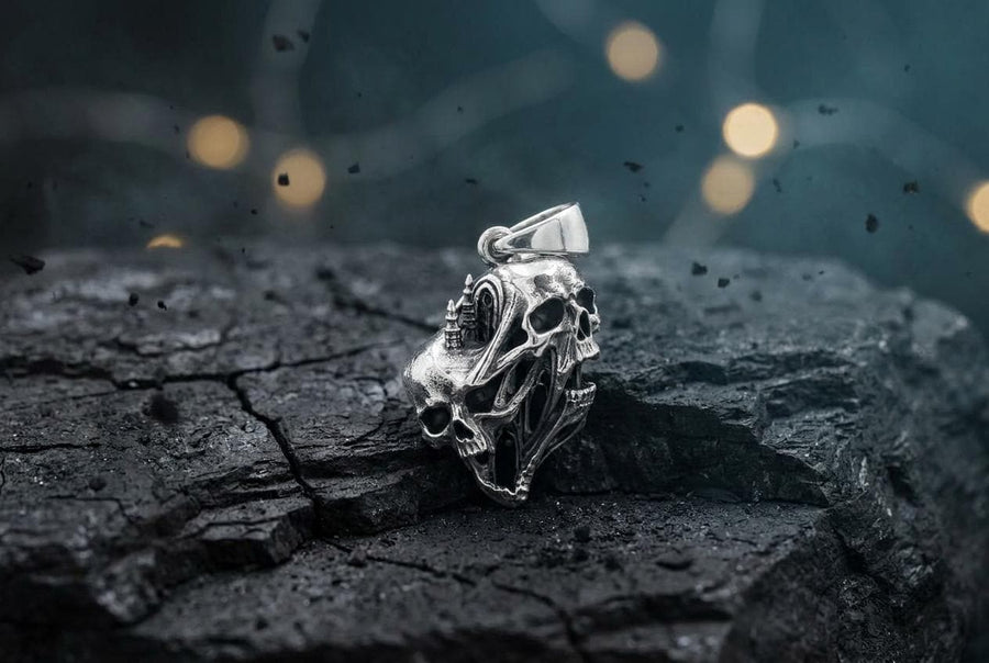 A side-profile view of the silver skull pendant showcases the breathtaking depth of the sculpted elements. The skulls appear stretched and elongated, morphing into each other. Dark oxidation heavily shadows the deeply recessed areas of the bone.