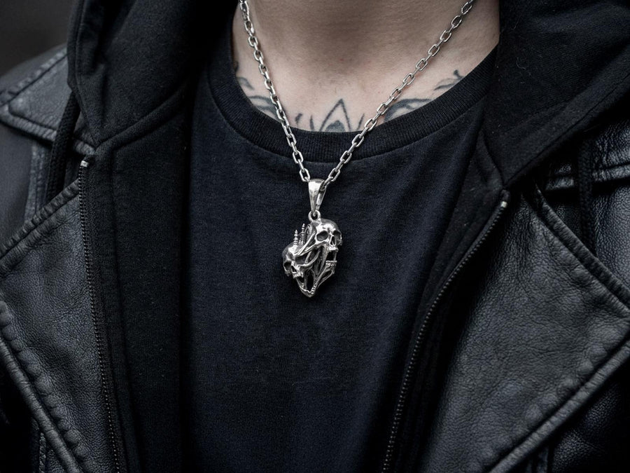 A side-profile view of the silver skull pendant showcases the breathtaking depth of the sculpted elements. The skulls appear stretched and elongated, morphing into each other. Dark oxidation heavily shadows the deeply recessed areas of the bone.