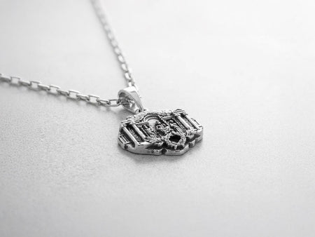 A close-up studio photograph of a 925 sterling silver Greek mythology pendant on a black background. The amulet features a detailed relief of a classical temple housing three figures - Poseidon, Zeus, and Athena. This striking pendant captures the majesty of Mount Olympus. Bright studio lighting illuminates the polished silver gods and temple columns, while pitch-black sulfur oxidation fills the deep crevices between the stone architecture.
