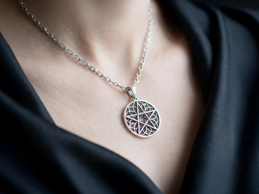 A close-up studio photograph of image_61ba46.png, a circular 925 sterling silver pendant on a black background. The design features a bold, sharp pentagram overlapping an intricate background of openwork gothic cathedral tracery and carved quatrefoil motifs. This striking artisan pendant captures the mesmerizing geometry of medieval architecture. Bright studio lighting illuminates the highly polished lines of the silver five-pointed star, contras