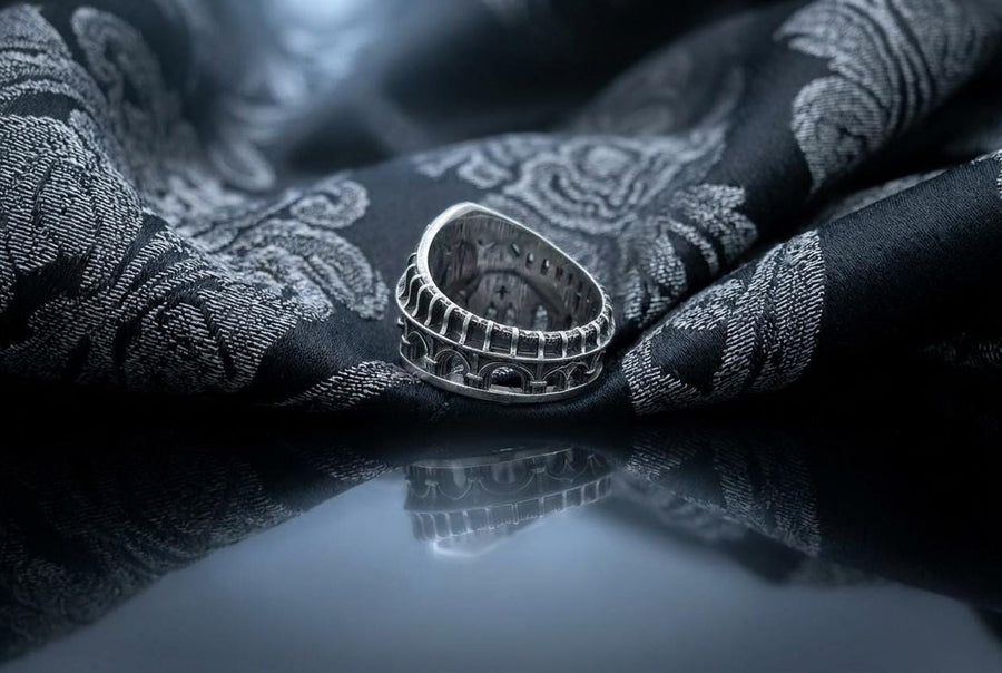 This striking artisan ring perfectly captures the monumental scale of medieval architecture. Bright studio lighting illuminates the polished silver arches and columns, contrasting beautifully with the deep, dark oxidation inside the hollow windows and recesses. Crafted from premium solid 925 sterling silver, this wide architectural band demonstrates the visual impact of an antiqued patina. Heavy sulfur oxidation settles into the intricate crevice