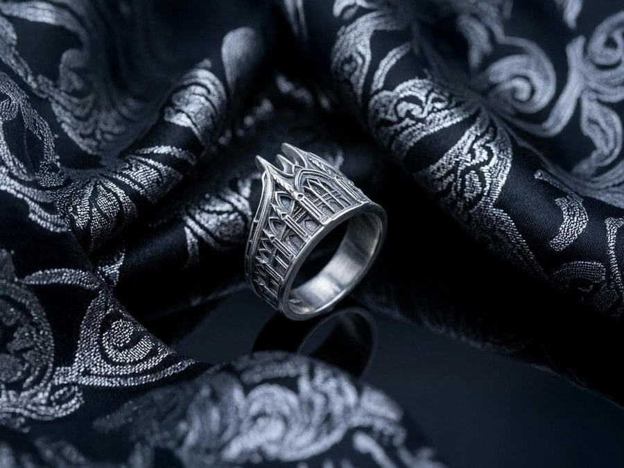 This solid 925 sterling silver gothic cathedral ring features soaring spires and intricately carved pointed arches. Resting on a grey surface, this oxidized silver band showcases detailed medieval tracery and classic stonework columns, perfect for a dark romance aesthetic. A striking 925 sterling silver architecture ring capturing the monumental scale of medieval sanctuaries. Bright lighting illuminates the polished silver gothic spires, contrast