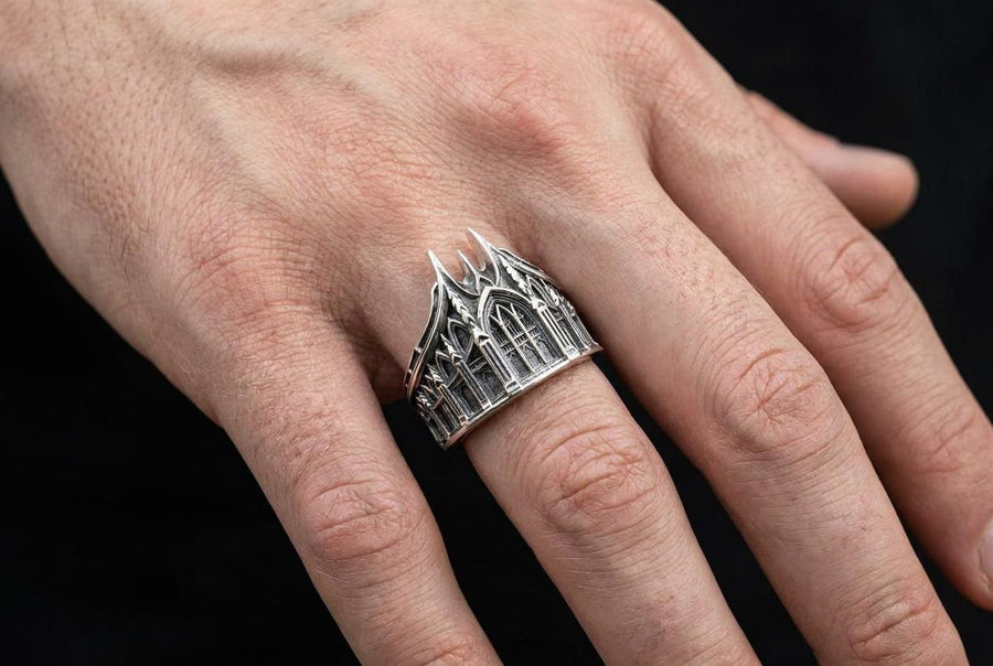 This solid 925 sterling silver gothic cathedral ring features soaring spires and intricately carved pointed arches. Resting on a grey surface, this oxidized silver band showcases detailed medieval tracery and classic stonework columns, perfect for a dark romance aesthetic. A striking 925 sterling silver architecture ring capturing the monumental scale of medieval sanctuaries. Bright lighting illuminates the polished silver gothic spires, contrast