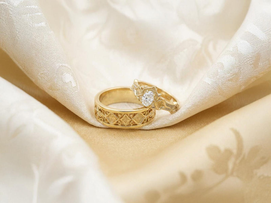 A close-up studio photograph of a matching 925 sterling silver gothic wedding ring set on a grey surface. The wide mens band and the delicate womens engagement ring both feature intricate medieval tracery and carved quatrefoils - highlighted by a dark oxidized background. This striking artisan bridal set perfectly captures the monumental scale of medieval architecture. Bright lighting illuminates the polished silver edges and the sparkling oval g