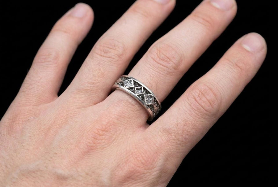 A close-up studio photograph of a matching 925 sterling silver gothic wedding ring set on a grey surface. The wide mens band and the delicate womens engagement ring both feature intricate medieval tracery and carved quatrefoils - highlighted by a dark oxidized background. This striking artisan bridal set perfectly captures the monumental scale of medieval architecture. Bright lighting illuminates the polished silver edges and the sparkling oval g