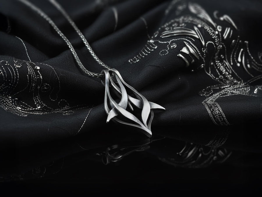 Solid sterling silver esoteric dagger drop charm held in hand, emphasizing the aggressive yet elegant lines. Close up of a man's fingers holding an abstract gothic spike amulet, highlighting the openwork silver design. Exceptional silversmithing is evident in this oxidized silver avant-garde necklace. The relief work perfectly balances the sharp lower points with smooth, sweeping interlaced upper curves. A bold modern statement piece for alte