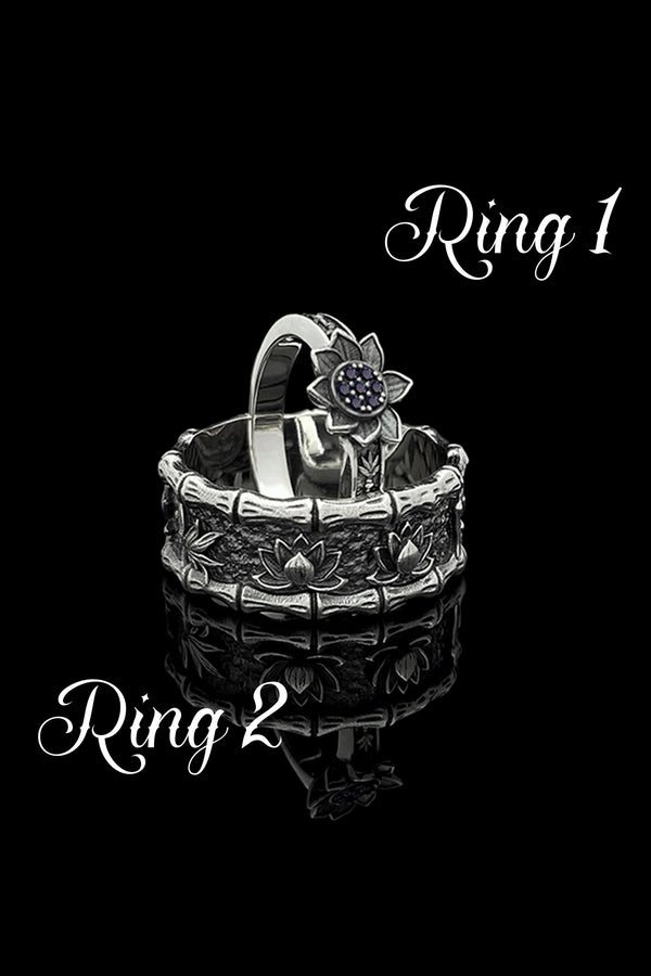 A close-up studio photograph of a matching 925 sterling silver botanical wedding ring set on a grey surface. The wide mens band features bamboo stalk edges and sculpted lotus flowers. The delicate womens engagement ring showcases a blooming lotus set with blue stones, highlighted by dark oxidation.