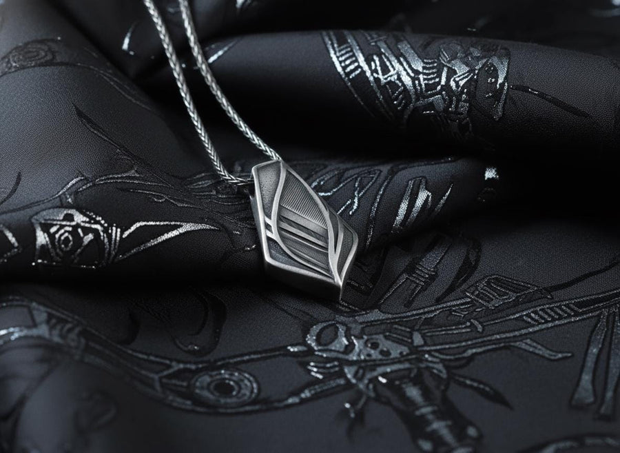 The pendant features a striking elongated shield silhouette, heavily detailed with precise micro-engraved lines and stippled textures that echo industrial elements. These darkened, oxidized recesses contrast brilliantly against the sharply polished, sweeping outer ridges. The multi-layered, armor-like plates give the piece incredible optical depth and a tactile, industrial feel.