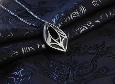 Dark fantasy silver eye pendant lying on black fabric, showing intricate openwork elven design and oxidized texture.