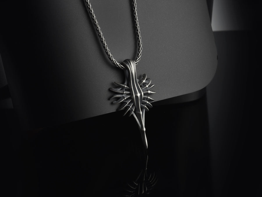Close-up of a man's hand holding a solid sterling silver alien weapon necklace, showing the sharp elongated drop.