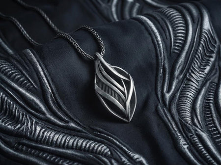 Dark fantasy silver teardrop pendant resting on black fabric, showing sweeping organic lines and an oxidized micro-ribbed background.