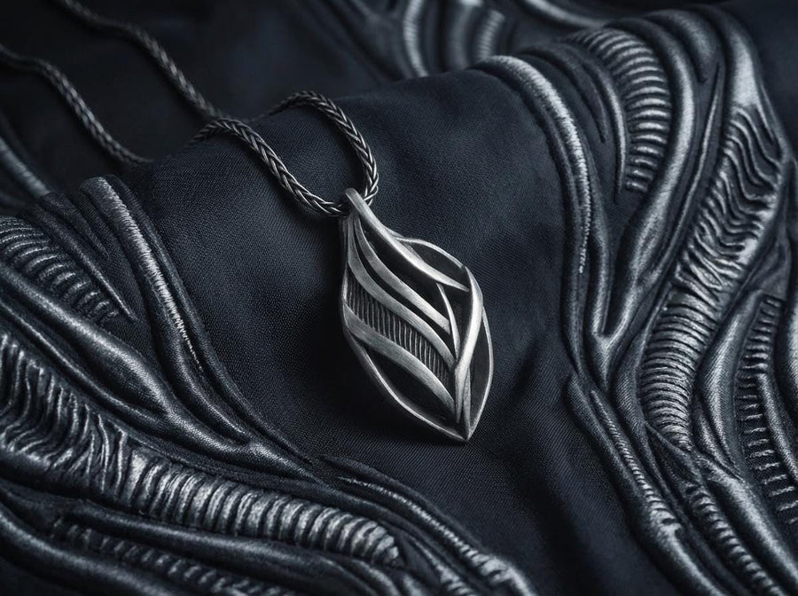 Dark fantasy silver teardrop pendant resting on black fabric, showing sweeping organic lines and an oxidized micro-ribbed background.
