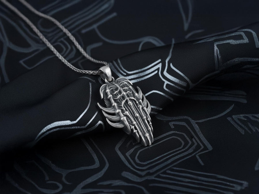 Close up of a man's hand holding a highly detailed gothic spine amulet, showing sharp silver claws and bone textures.