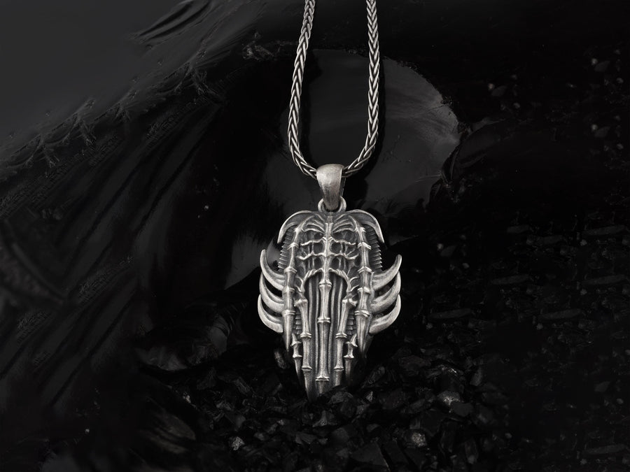 Close up of a man's hand holding a highly detailed gothic spine amulet, showing sharp silver claws and bone textures.