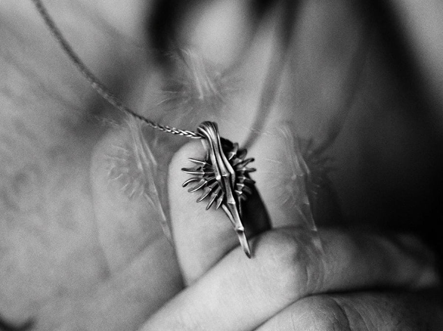 Close-up of a man's hand holding a solid sterling silver alien weapon necklace, showing the sharp elongated drop.