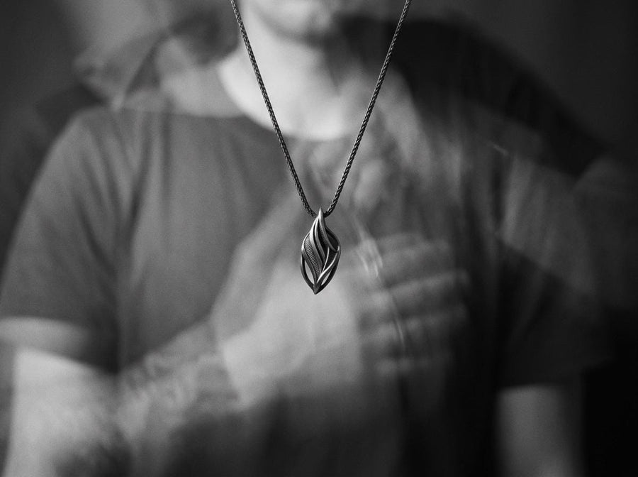 Dark fantasy silver teardrop pendant resting on black fabric, showing sweeping organic lines and an oxidized micro-ribbed background.