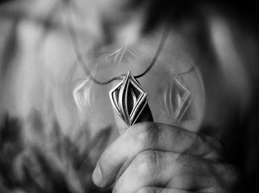 Dark sci-fi silver rhombus pendant glowing softly amid smoke, showcasing a 3D architectural design with parallel inner beams.