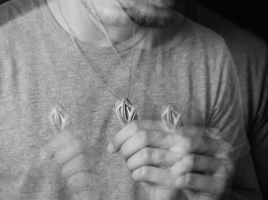 Dark sci-fi silver rhombus pendant glowing softly amid smoke, showcasing a 3D architectural design with parallel inner beams.