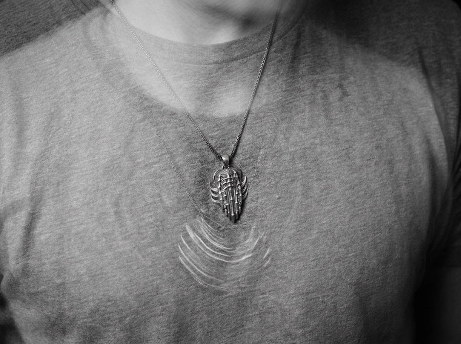 Close up of a man's hand holding a highly detailed gothic spine amulet, showing sharp silver claws and bone textures.