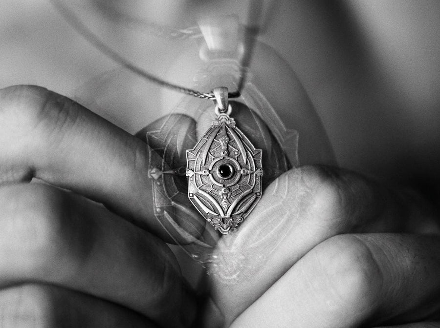 Unique artisan crafted silver armor necklace for men, fantasy sci-fi jewelry, A close-up studio photograph of a 925 sterling silver shield pendant resting on a dark reflective surface. The avant-garde design features geometric plating and a central circular core, highlighted by a dark matte oxidized finish. This striking artisan pendant captures the essence of futuristic armor.