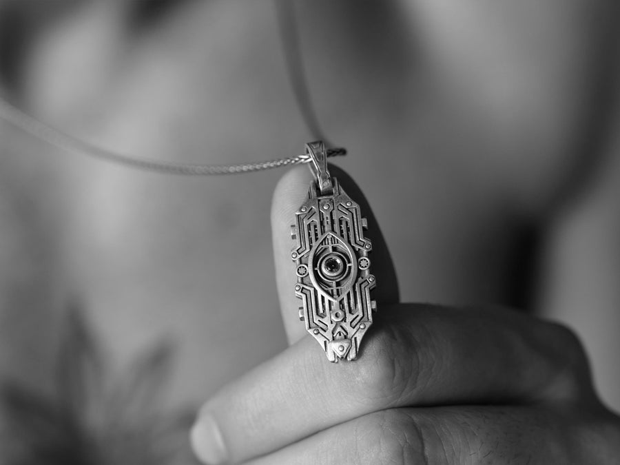 Intricate cyberpunk design inspired by high-tech circuitry and sci-fi artifacts. Exceptional silversmithing is evident in this oxidized silver avant-garde necklace. The relief work perfectly balances the sharp lines of the outer mechanical border with the central red gemstone core. A bold cyberpunk statement piece for alternative collectors.