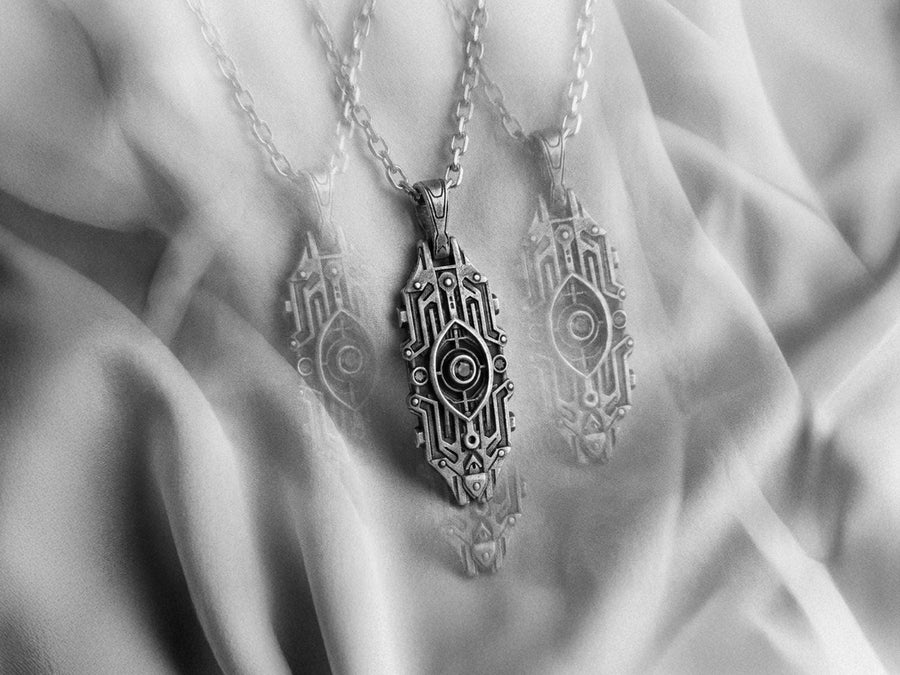 Intricate cyberpunk design inspired by high-tech circuitry and sci-fi artifacts. Exceptional silversmithing is evident in this oxidized silver avant-garde necklace. The relief work perfectly balances the sharp lines of the outer mechanical border with the central red gemstone core. A bold cyberpunk statement piece for alternative collectors.