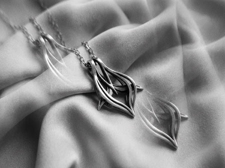 May include: A silver-toned metal pendant necklace featuring an abstract, multi-layered design with curved, flowing lines and a dark, oxidized finish in the recessed areas. The pendant is attached to a matching silver-toned link chain necklace.